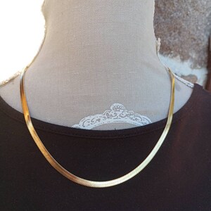 Peut inclure: Un collier de chaîne serpent en or sur un mannequin portant un t-shirt noir.