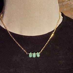 Pode incluir: Um colar de corrente de ouro com três pedras verdes em forma de lágrima.