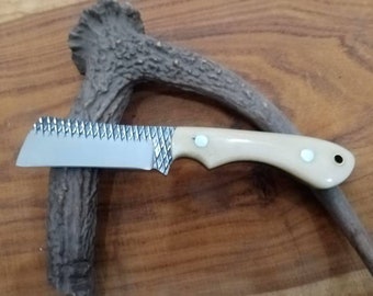 May include: A small, white-handled knife with a serrated blade and a diamond-patterned finish. The knife is resting on a piece of antler.