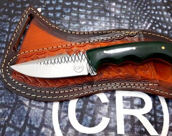 May include: A small, stainless steel knife with a green handle and a serrated blade. The knife is in a brown leather sheath with decorative stitching.