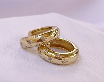 May include: A pair of gold hoop earrings with a starburst design and small clear stones.