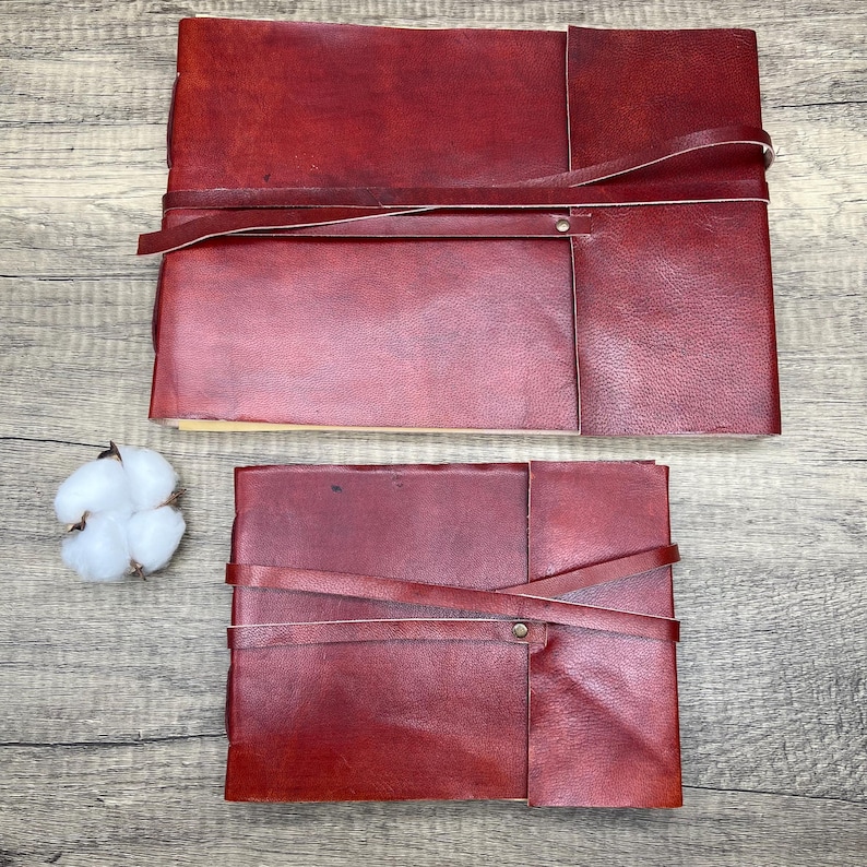 May include: Two burgundy leather journals with straps and metal clasps. The larger journal is on top of the smaller journal.