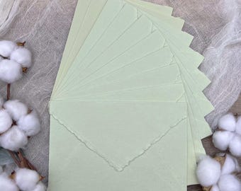 May include: A stack of light green envelopes with a deckled edge. The envelopes are arranged in a fan shape and are made of a textured paper.