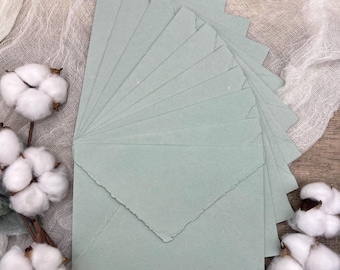 May include: A stack of light blue envelopes with deckled edges. The envelopes are arranged in a fan shape and are made of a textured paper.
