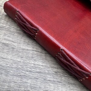 May include: A close-up of a burgundy leather-bound journal with brown stitching along the spine.