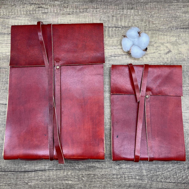 May include: Two red leather journals with a strap closure. The journals are tied together with a leather strap.