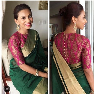 May include: A woman wearing a green saree with a gold border and a pink blouse with a paisley pattern. The blouse has a button-up back.