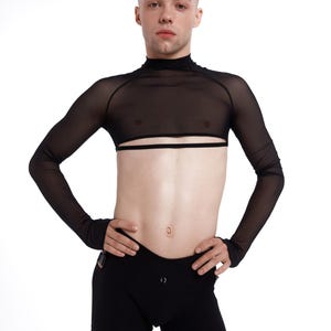 Könnte beinhalten: Schwarzes Mesh-Langarm-Crop-Top mit hohem Ausschnitt und horizontalem Ausschnitt über der Brust. Das Model trägt auch schwarze Shorts. Das Outfit ist für Tanz- oder Bühnenauftritte konzipiert.