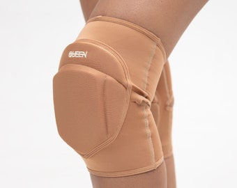May include: A pair of tan knee pads with a padded section on the front. The knee pads have a white logo that says "QUEEN" on the front.
