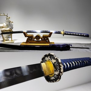 May include: A traditional Japanese katana sword with a black scabbard and a blue and white patterned handle. The sword is displayed on a wooden stand with intricate carvings.
