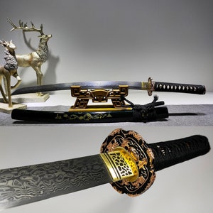 May include: A black katana sword with a gold-coloured hilt and a black scabbard. The sword is resting on a wooden stand with a gold-coloured design. The sword is decorated with a gold-coloured pattern.