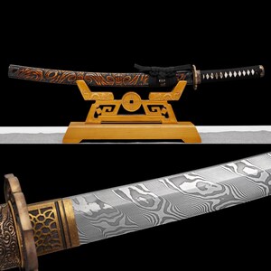 Pode incluir: Uma espada katana japonesa exibida em um suporte de madeira decorativo. A espada apresenta uma empunhadura preta com um padrão de diamante e uma lâmina estampada. A bainha é preta com detalhes em laranja e dourado. O suporte é marrom claro com um detalhe em forma de moeda.