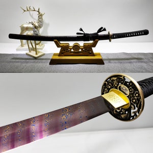 Pode incluir: Uma katana preta com uma pega dourada e uma tsuba decorativa. A espada é exibida num suporte de madeira com um design dourado.