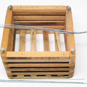 May include: A wooden hanging planter with a wire hook and three wire hangers. The planter is made of natural wood and has a rectangular shape.