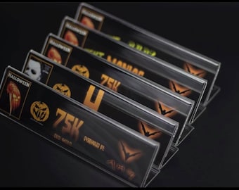 May include: A set of six black acrylic display stands with orange and gold Halloween themed designs. The stands feature a pumpkin, a bat, and a knife. The text "Halloween" and "75K" are visible on the stands.