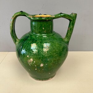 Puede incluir: Una jarra de cerámica verde con una boca ancha y un asa. La jarra tiene un borde amarillo y un esmalte verde moteado.