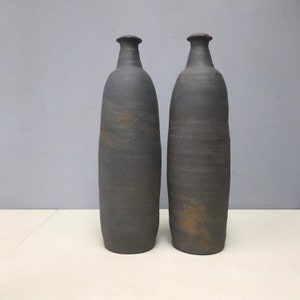 Peut inclure: Deux grands vases en céramique gris foncé avec une surface texturée légèrement rugueuse. Les vases ont une forme arrondie, légèrement bulbeuse et une ouverture étroite en haut.
