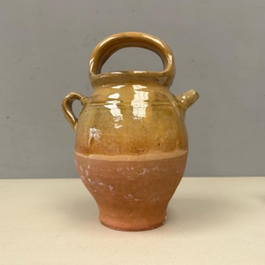 Puede incluir: Jarra de cerámica rústica de dos tonos con un asa grande y un pico. La parte superior es de un cálido amarillo-marrón, mientras que la mitad inferior es de color marrón rojizo. La jarra tiene un asa pequeña en el lateral.