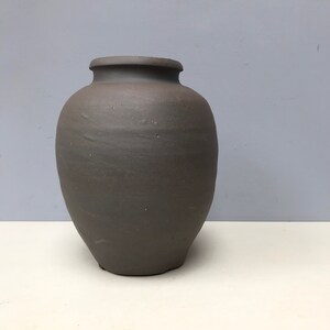 Peut inclure: Un vase en céramique brun foncé avec un corps arrondi et une ouverture légèrement évasée. Le vase a une finition lisse et mate.
