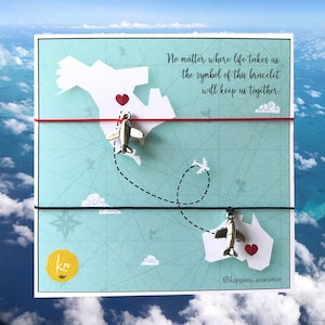 May include: A red and black string bracelet with two silver airplane charms and a red heart charm. The bracelet is tied around a card with the text "No matter where life takes us, the symbol of this bracelet will keep us together." and the text "@kappanu.accesorios".