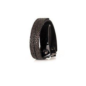 May include: A black leather bracelet with a textured design and a silver buckle.
