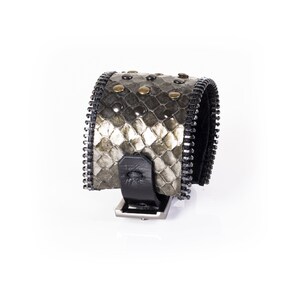 May include: A black and gray zippered bracelet with a snakeskin pattern and silver studs.