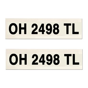 May include: Two rectangular stickers with the text "OH 2498 TL" in bold black font. The background of the stickers is a light beige color. The stickers are likely for a vehicle or similar application.