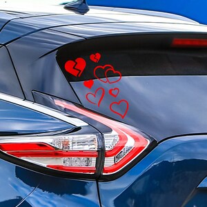 Può includere: Un'auto blu con un adesivo a forma di cuore rosso sul lunotto posteriore. L'adesivo è composto da diversi cuori, tra cui un cuore spezzato.