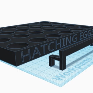May include: A black plastic egg incubator with 25 circular holes and the text "HATCHING EGGS" on the front. A small black bench is in front of the incubator.