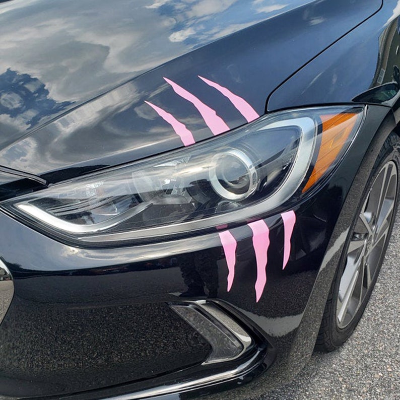 Op de afbeelding: Een zwarte auto met roze klauwen op de voorbumper. De auto heeft een zilveren voorbumper en een zilveren wiel.