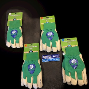 May include: Four pairs of green work gloves with white leather palms. The gloves have a blue alien logo with a snowflake on the back. The gloves are labeled with sizes S, M, L, and XL. The packaging says "Discover your peak with Other Orbits".