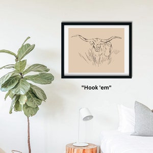 May include: A black framed print with a beige background featuring a line drawing of a longhorn steer with large horns. The text "Hook 'em" is printed below the image.