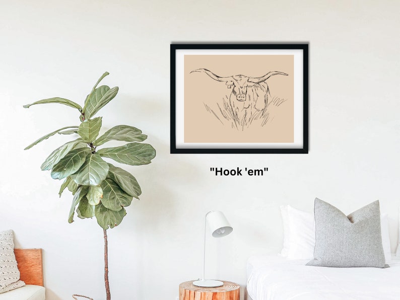 May include: A black framed print with a beige background featuring a line drawing of a longhorn steer with large horns. The text "Hook 'em" is printed below the image.