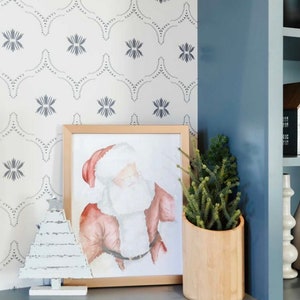 May include: A framed watercolor painting of Santa Claus with a white beard and red suit, a white wooden Christmas tree, and a potted green plant in a wooden planter on a gray surface.