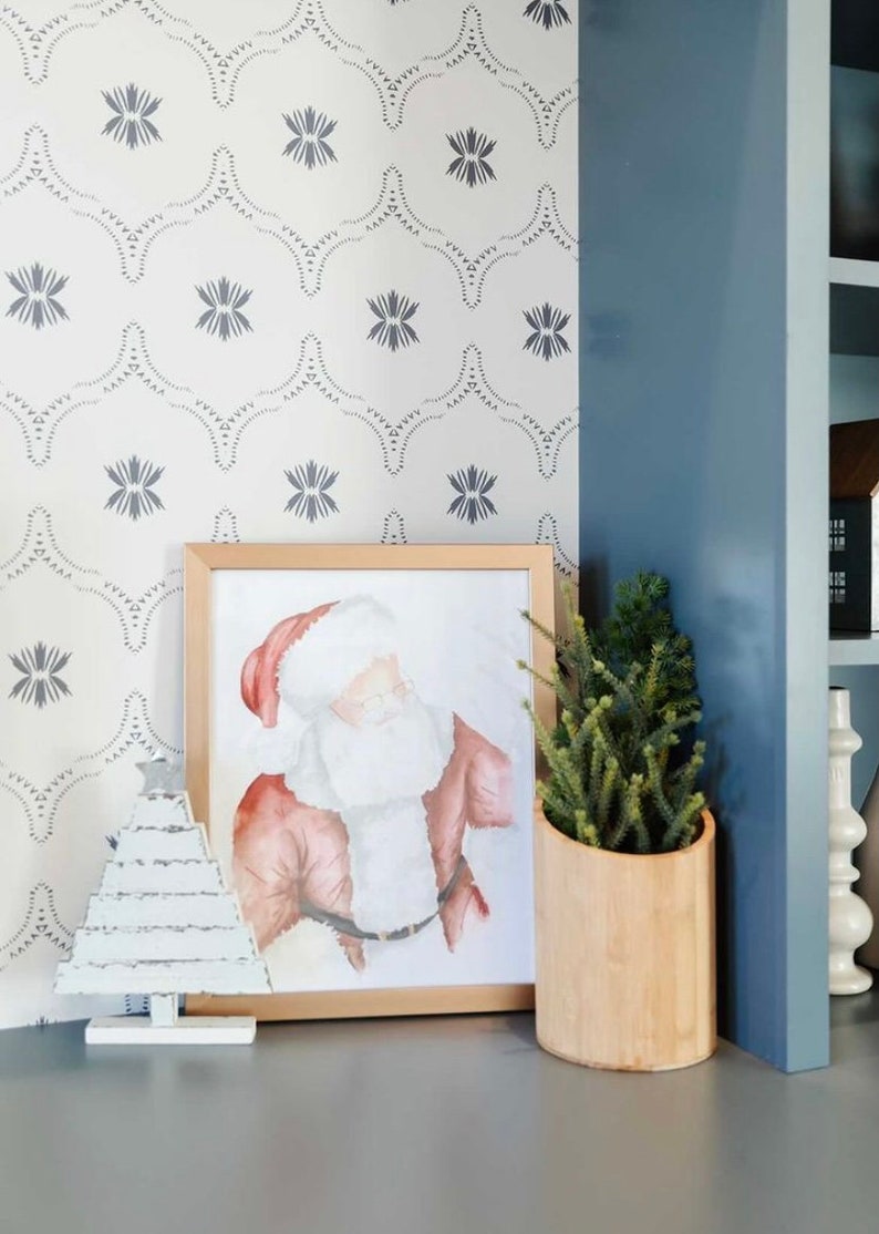 May include: A framed watercolor painting of Santa Claus with a white beard and red suit, a white wooden Christmas tree, and a potted green plant in a wooden planter on a gray surface.