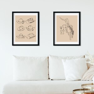 May include: Two framed black and white line drawings. The first drawing shows six cowboy hats. The second drawing shows a cowboy riding a bucking horse.