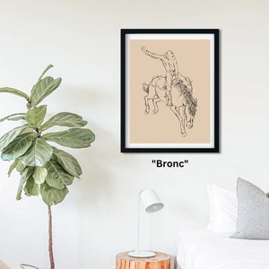 May include: A black and white line drawing of a cowboy riding a bucking bronco. The drawing is on a beige background and framed in black. The text "Bronc" is below the frame.