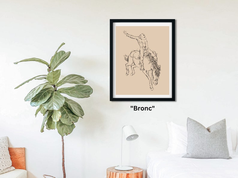 May include: A black and white line drawing of a cowboy riding a bucking bronco. The drawing is on a beige background and framed in black. The text "Bronc" is below the frame.