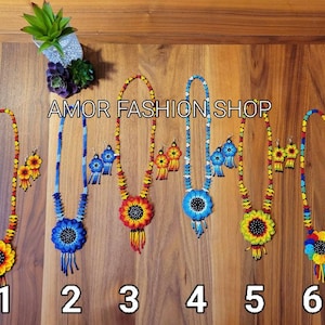 May include: Six sets of beaded necklaces and matching earrings, each featuring a large sunflower-shaped pendant with a black center. The jewelry sets display various color combinations including red, yellow, blue, and orange beads. Text reads AMOR FASHION SHOP.