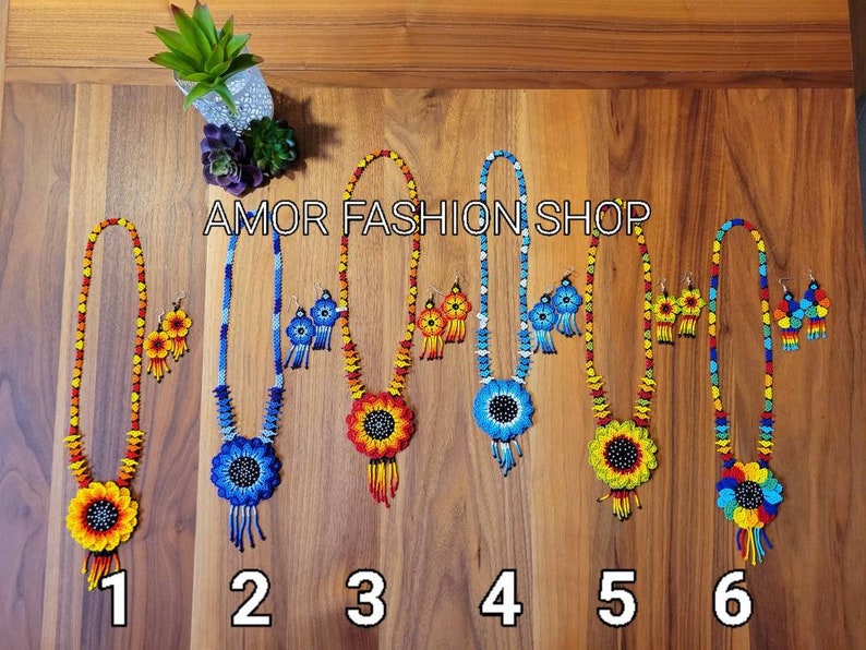 May include: Six sets of beaded necklaces and matching earrings, each featuring a large sunflower-shaped pendant with a black center. The jewelry sets display various color combinations including red, yellow, blue, and orange beads. Text reads AMOR FASHION SHOP.