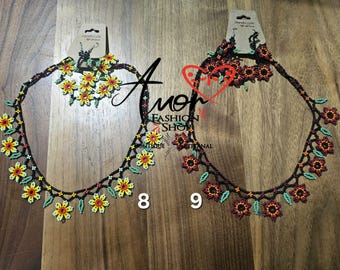 May include: Two beaded necklace and earring sets. One set features yellow and orange flower designs with green leaves, the other has red and orange flower designs with green leaves. Both sets are on a wooden surface.