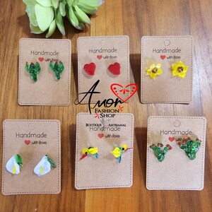 May include: Six cards with handmade earrings on them. The earrings are made of glass and feature different designs, including cacti, hearts, flowers, hummingbirds, and calla lilies. The cards are all brown and have the words "Handmade with love" on them.
