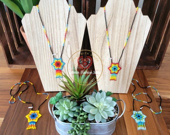 May include: Four beaded necklaces with colourful flower pendants. The necklaces are displayed on wooden stands and a small potted plant is in the centre of the image. The text "Made with Amor" and "Amor Fashion Store" is visible in the image.