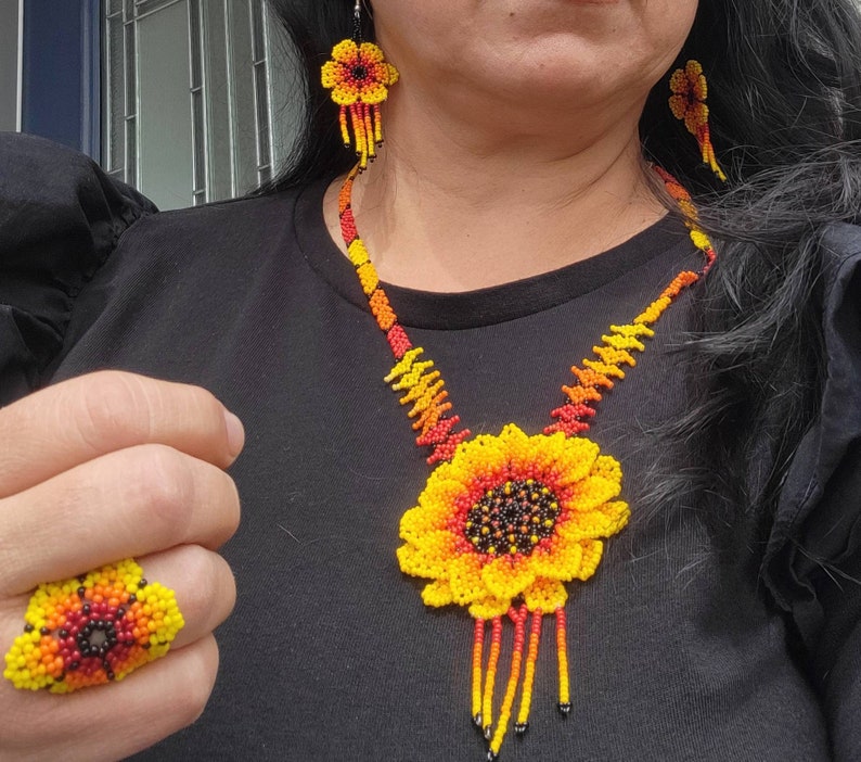 May include: A beaded jewelry set featuring a sunflower-shaped pendant necklace, matching flower-shaped drop earrings, and a flower-shaped ring. The pieces are crafted with small yellow, orange, red, and black beads in a vibrant floral pattern.