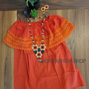 May include: An orange off-the-shoulder blouse featuring a wide lace trim along the neckline, paired with a matching beaded necklace and earrings set. The jewelry displays a floral pattern in white, yellow, orange, and black. Text reads AMOR FASHION SHOP.