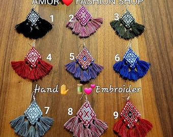 May include: Nine pairs of handmade embroidered tassel earrings in various colors, including black, pink, green, red, blue, and gray. Each earring features a diamond-shaped design and a long tassel. The text "AMOR FASHION SHOP" is visible.