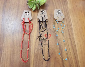 Puede incluir: Tres juegos de collares de cuentas superpuestos con pendientes a juego. Los collares están hechos con cuentas rojas, negras y azules con detalles dorados. Los pendientes son pequeños y tienen un diseño de flor.