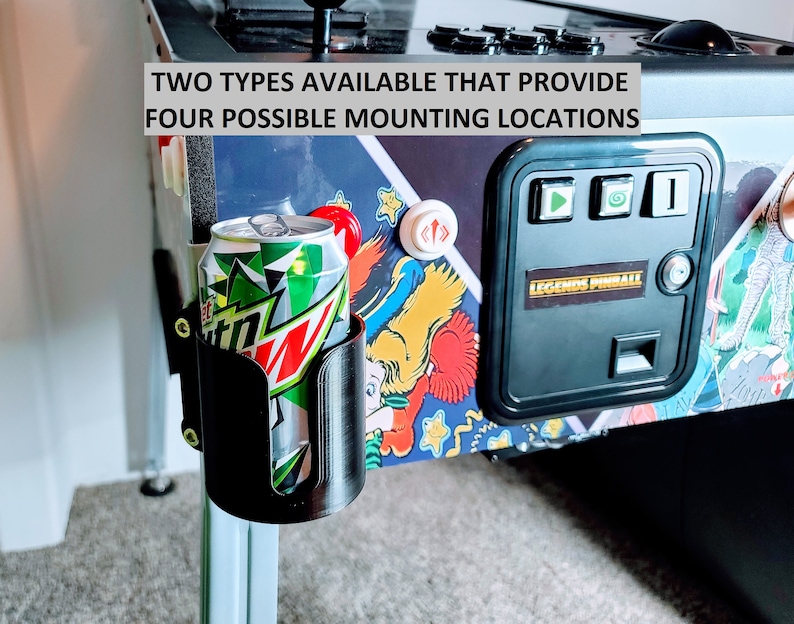 May include: A black plastic drink holder attached to a pinball machine. The holder is designed to hold a can of soda or a bottle of water. The text "TWO TYPES AVAILABLE THAT PROVIDE FOUR POSSIBLE MOUNTING LOCATIONS" is visible on the pinball machine.