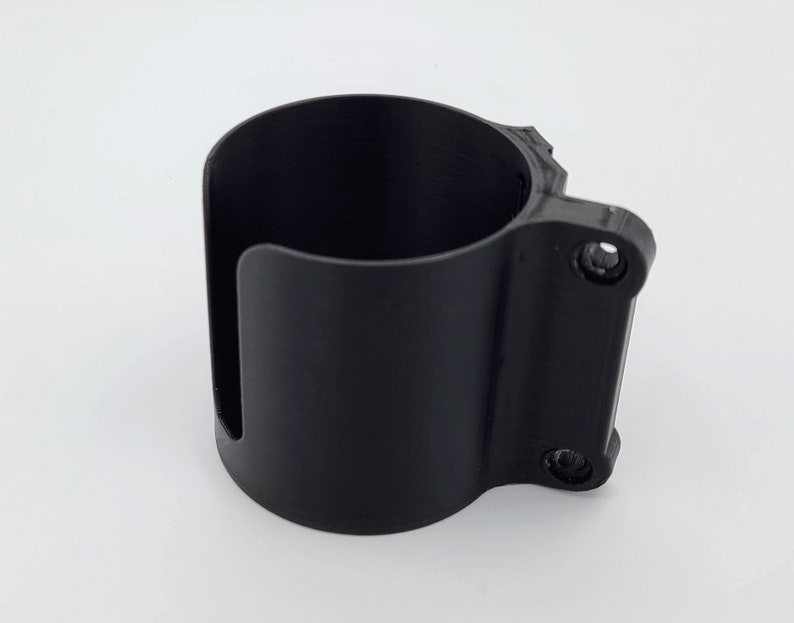 May include: A black plastic cup holder with two screws on the side. The holder is designed to attach to a surface.