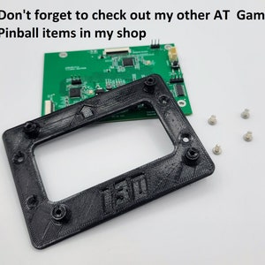 May include: A black plastic frame with a cutout for a screen. The frame has four screw holes and the text "130" is visible on the bottom. There are four small silver screws on a white surface.